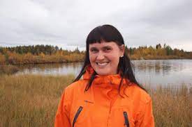 Paula katsoo kameraan ja hymyilee vesistön äärellä. 