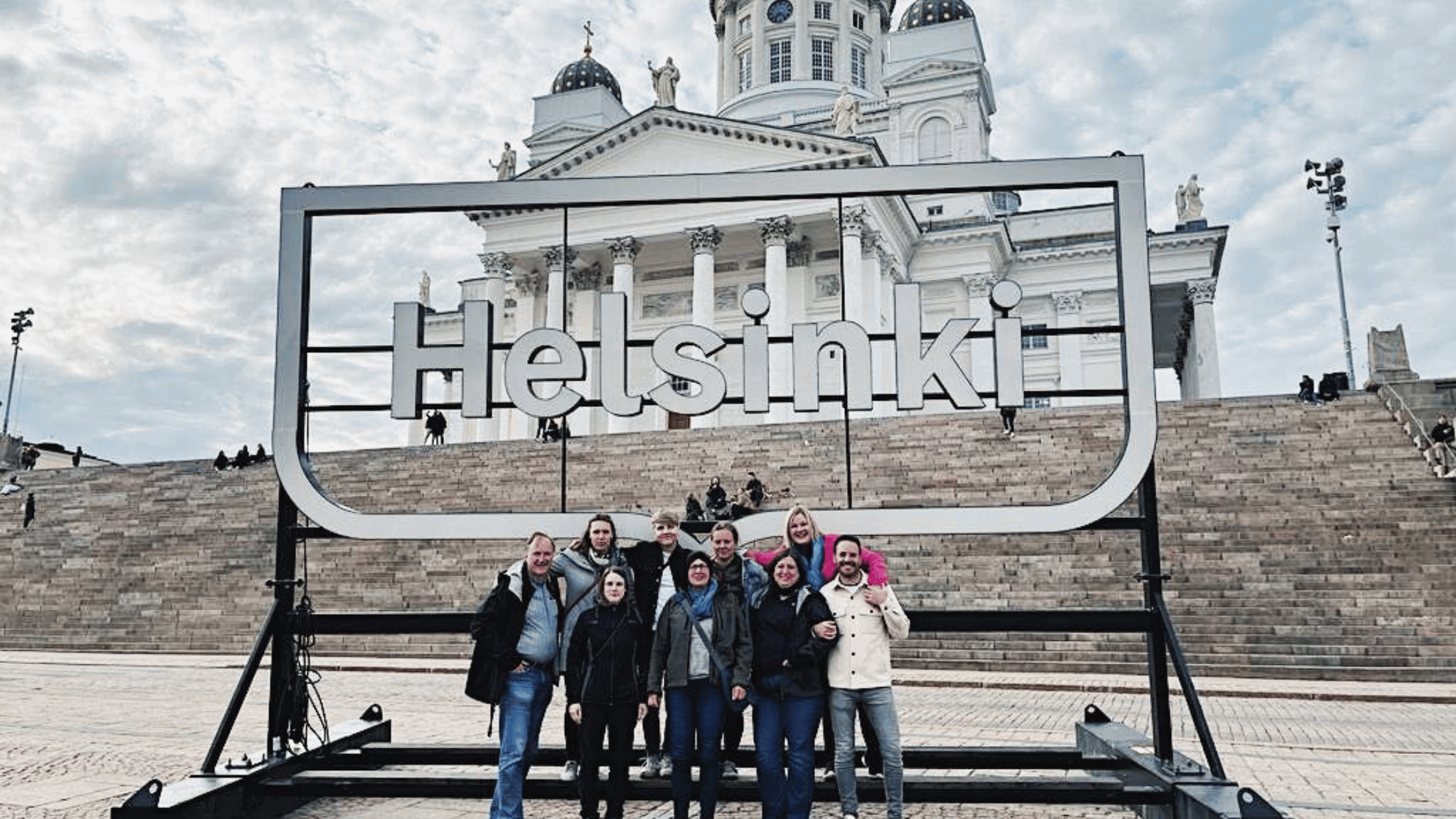 Matkanjärjestäjät ryhmänä senaatintorilla Helsinki-valokyltin edessä. 