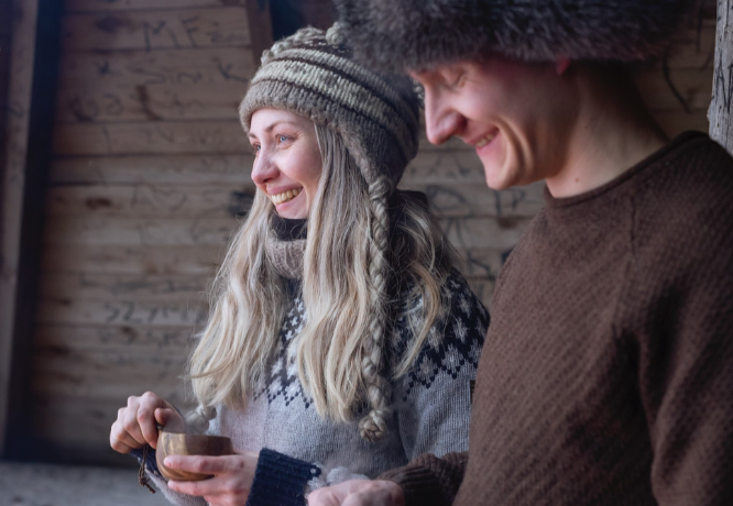 Mies ja nainen ovat pukeutuneet lämpimiin, murretun sävyisiin neuleisiin ja pipoihin. 