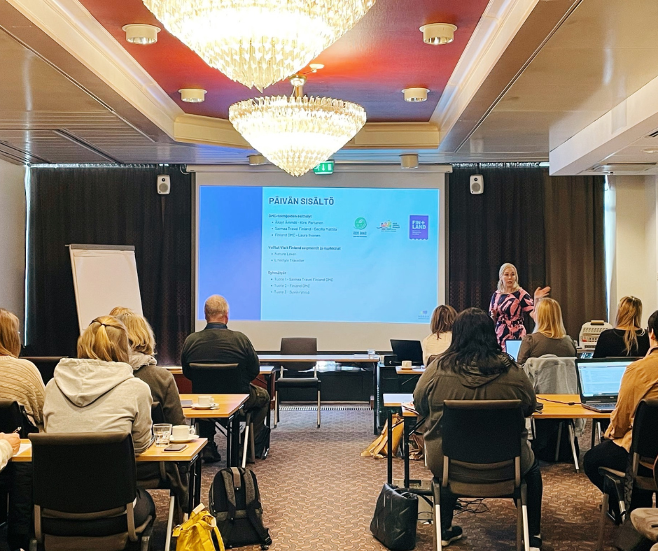 Kouluttaja esittelee matkailutyöpajan ohjelmaa osallistujille valkokankaalla.