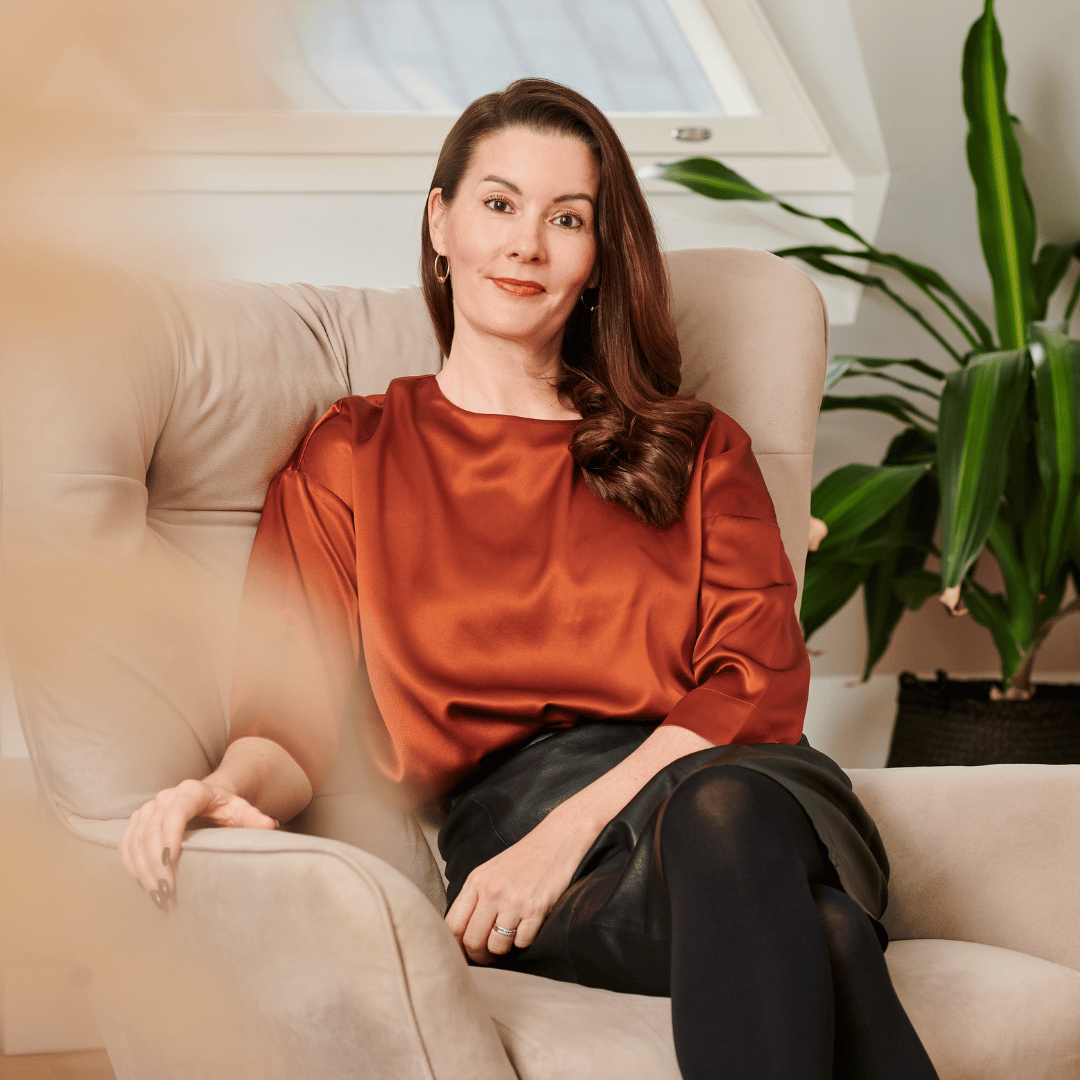 Greta Tanskanen katsoo kameraan ja hymyilee oman kotinsa nojatuolissa kuvattuna. 