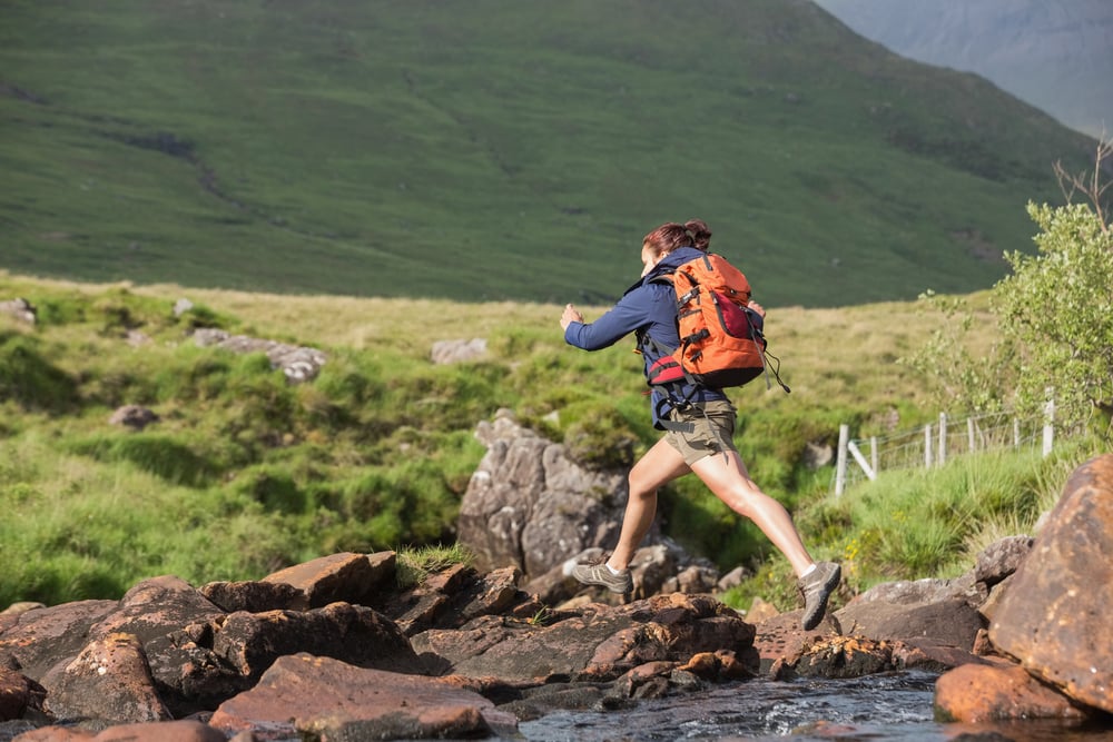 Athletic hiker leaping across rocks in a river in the countryside-4
