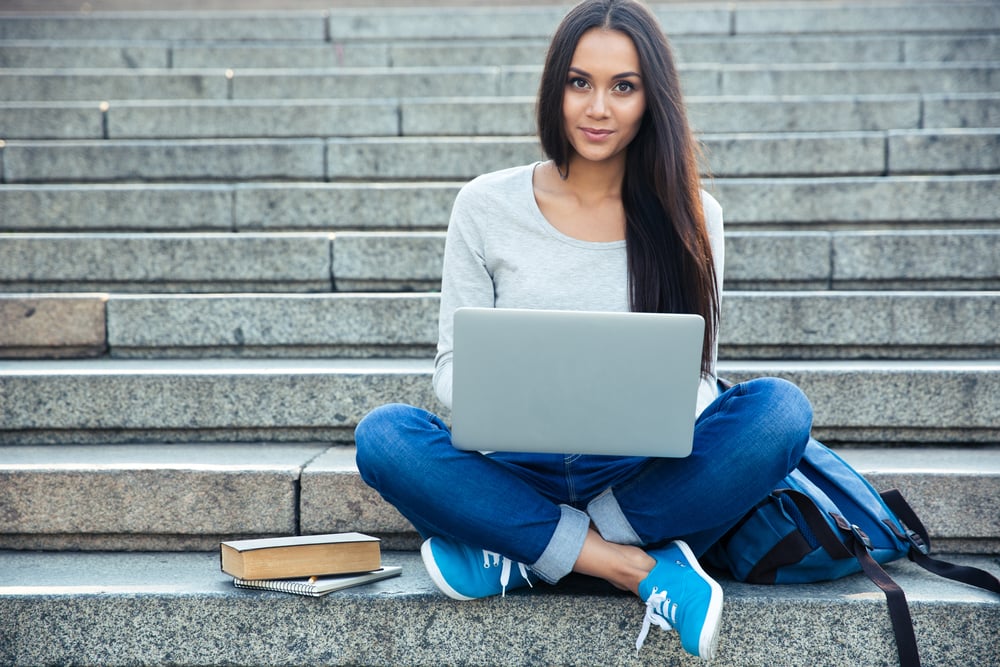 Portrait of a happy young woman sitting on the city stairs and using laptop computer outdoors-1
